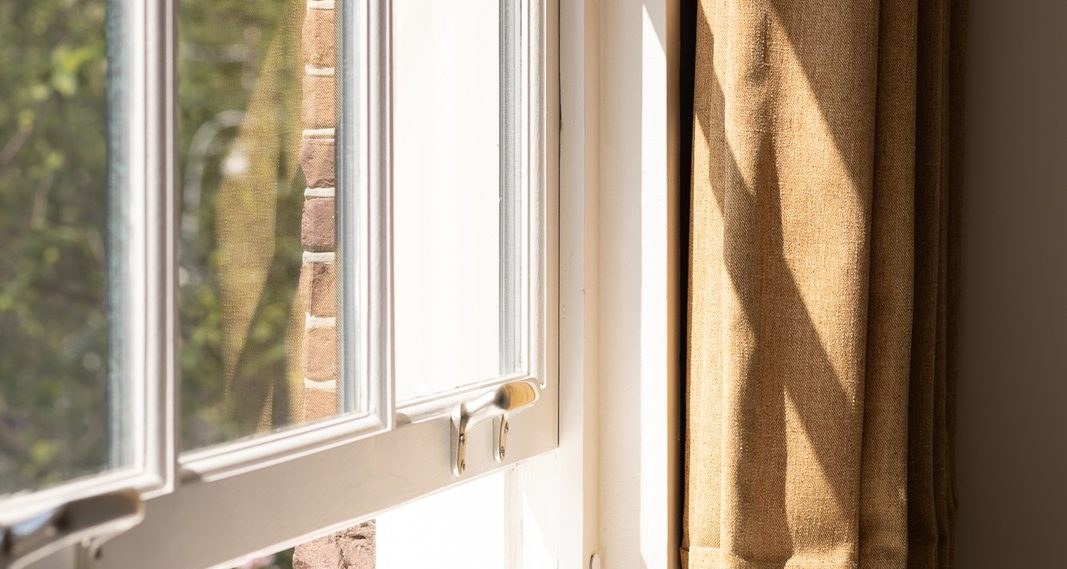 Open sash window with brass lifts and a linen curtain